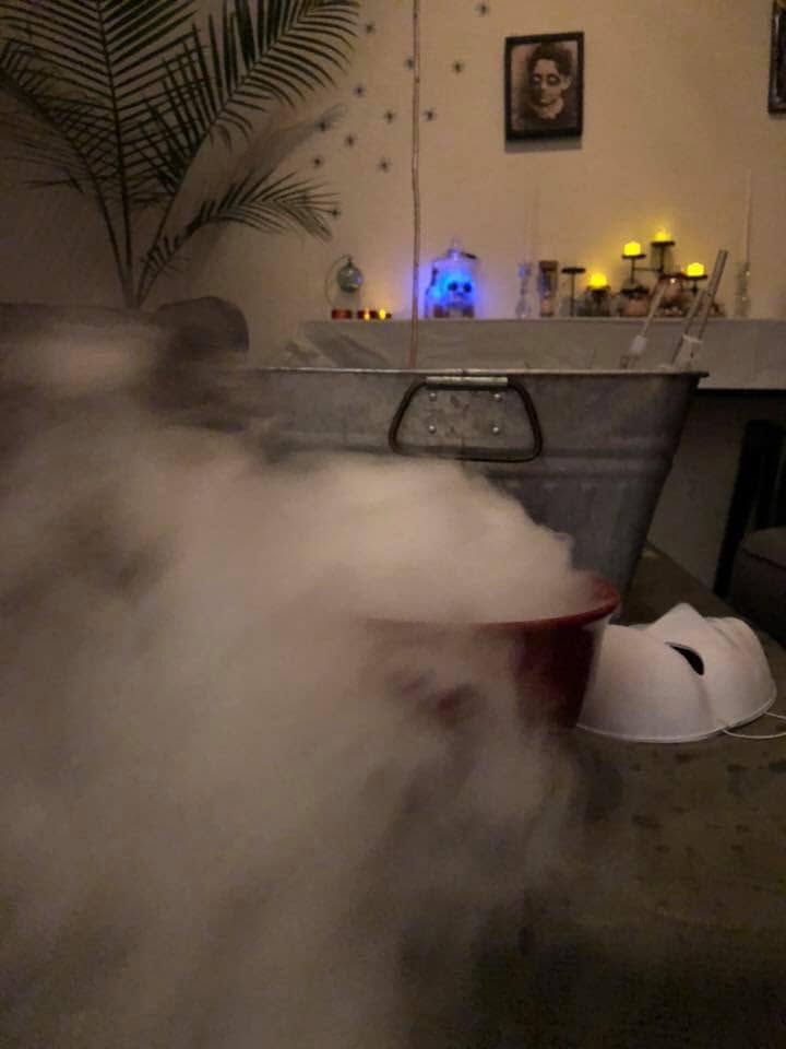 A smoking cauldron-like bowl in front of a galvanized tub and candlelit decorations at The Witch House in 2018