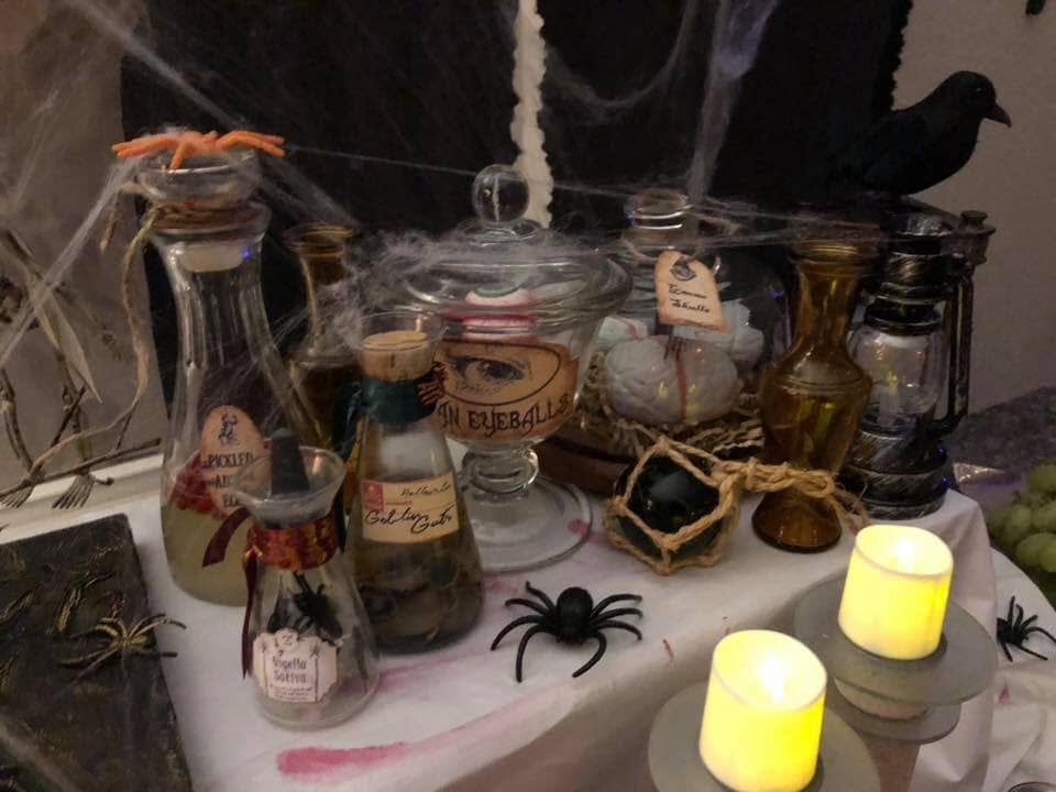An apothecary-style Halloween display with labeled bottles, eyeballs, candles, and cobwebs at The Witch House in 2018