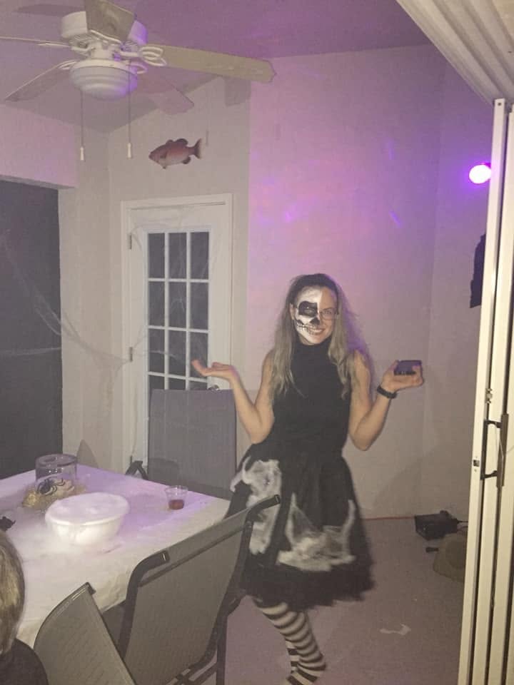 A guest with half-skull face paint and a dark dress posing in a softly lit room at The Witch House in 2018