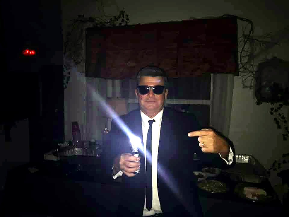 A sharply dressed guest in sunglasses holding a bright light at The Haunted Tavern in 2019