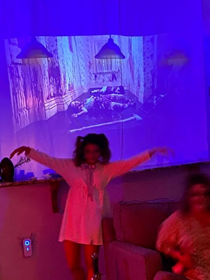 A guest in a white nightgown performing beneath a projected haunted room scene at the 2020 Halloween party