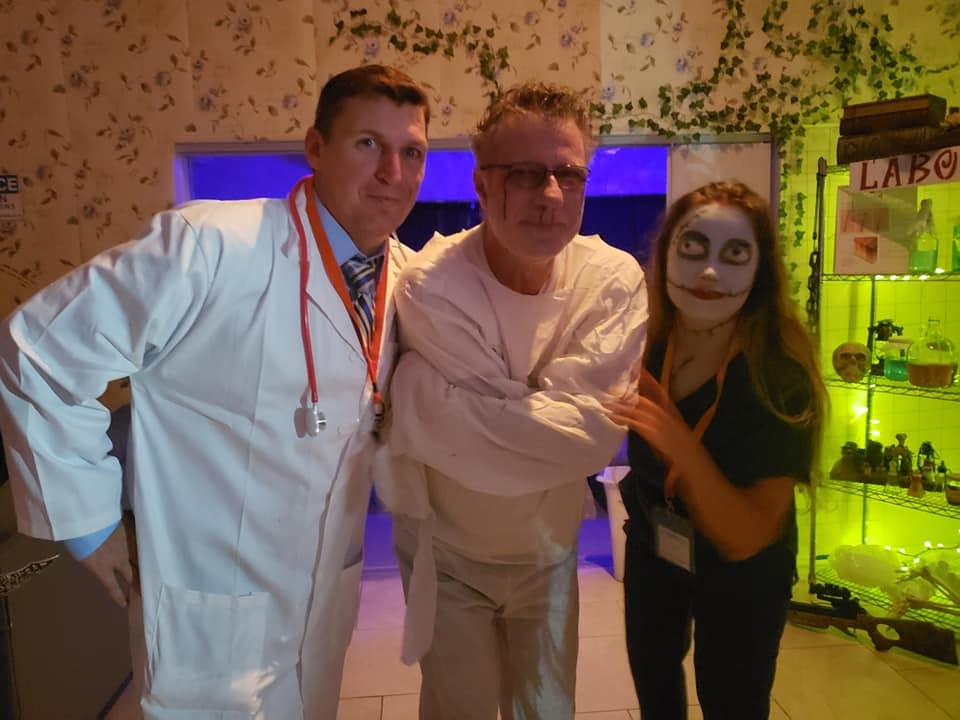 Three guests including a doctor, a patient in a straitjacket, and an eerie nurse posing in the laboratory at the 2020 Halloween party