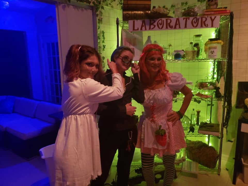Three guests posing in front of the laboratory set dressed as haunted asylum characters at the 2020 Halloween party