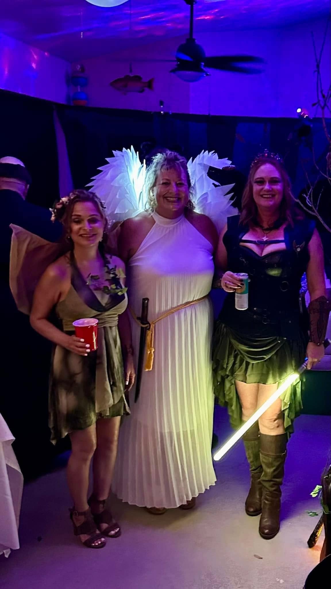 Three costumed women posing together including an angelic figure at the 2023 party