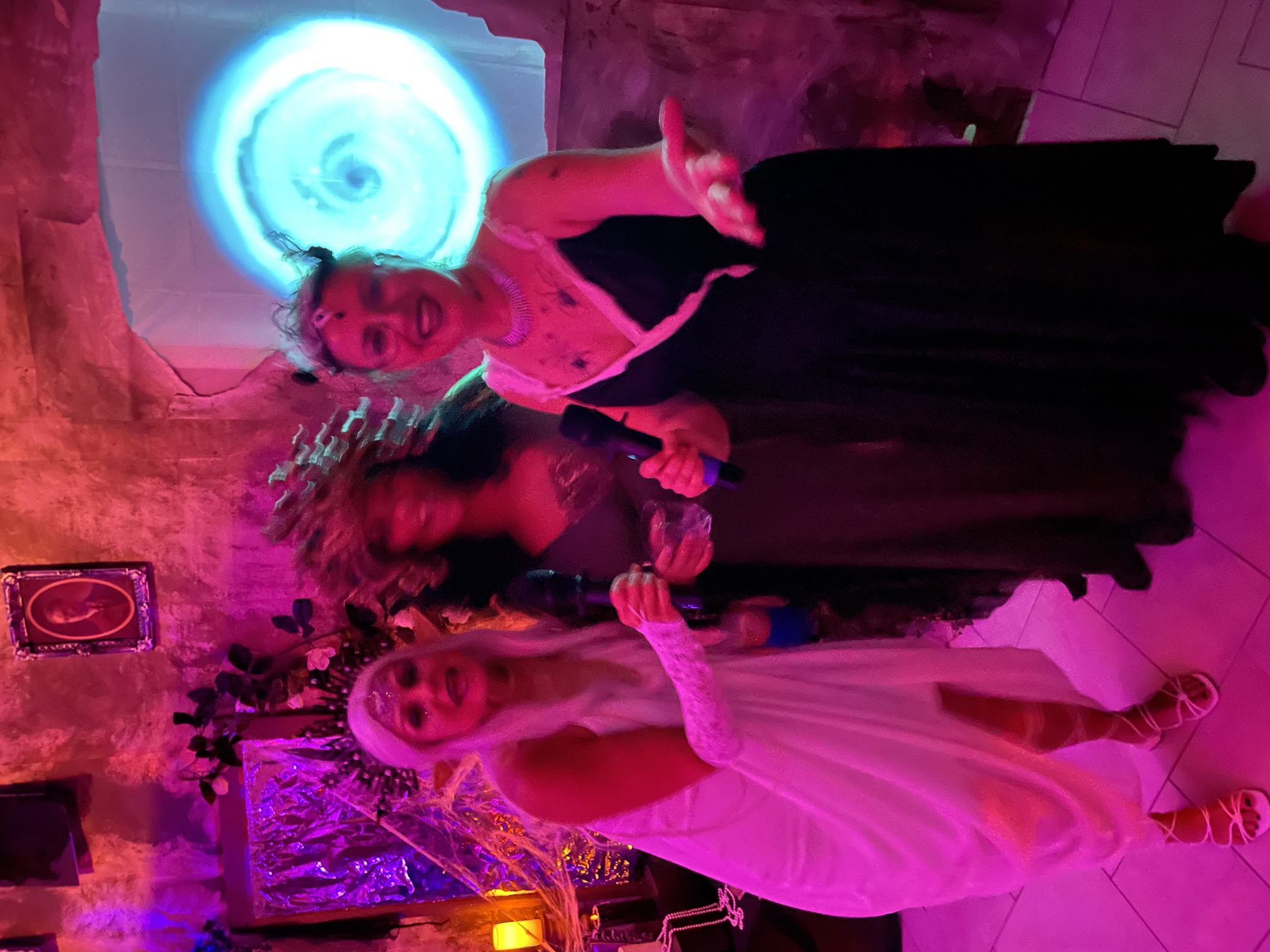 Three costumed women with microphones singing before the portal at the 2024 party