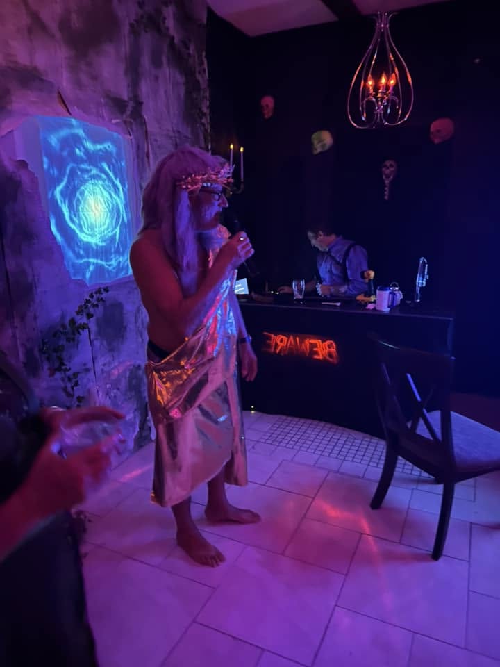 A guest in shimmering robes addressing the room with a microphone at the 2024 party
