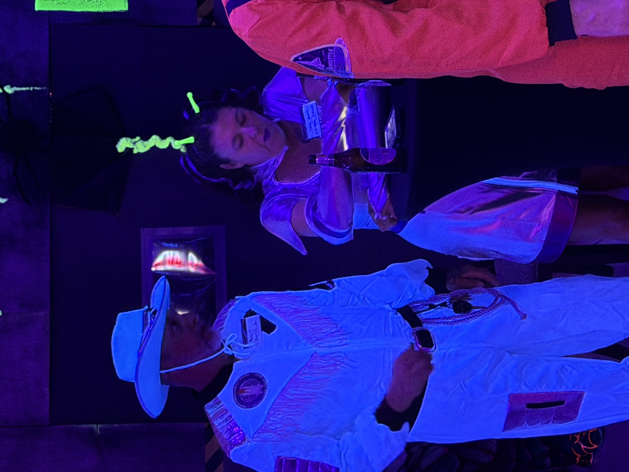 Two guests in luminous western and alien-inspired costumes standing together in blacklight at The Space Station in 2025