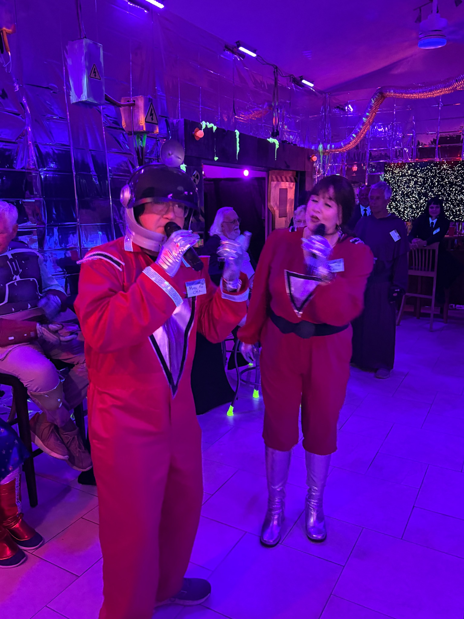 Two performers in matching red retro-space suits singing into microphones at The Space Station in 2025