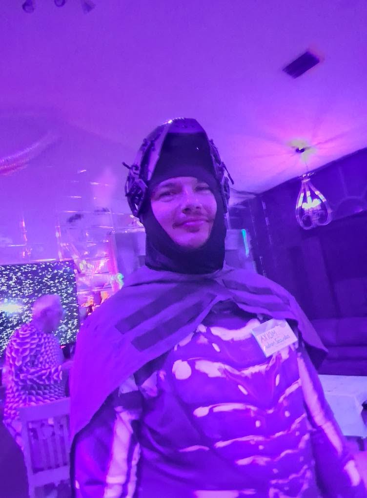A portrait of a guest in a bat-like sci-fi costume glowing beneath violet party lights at The Space Station in 2025
