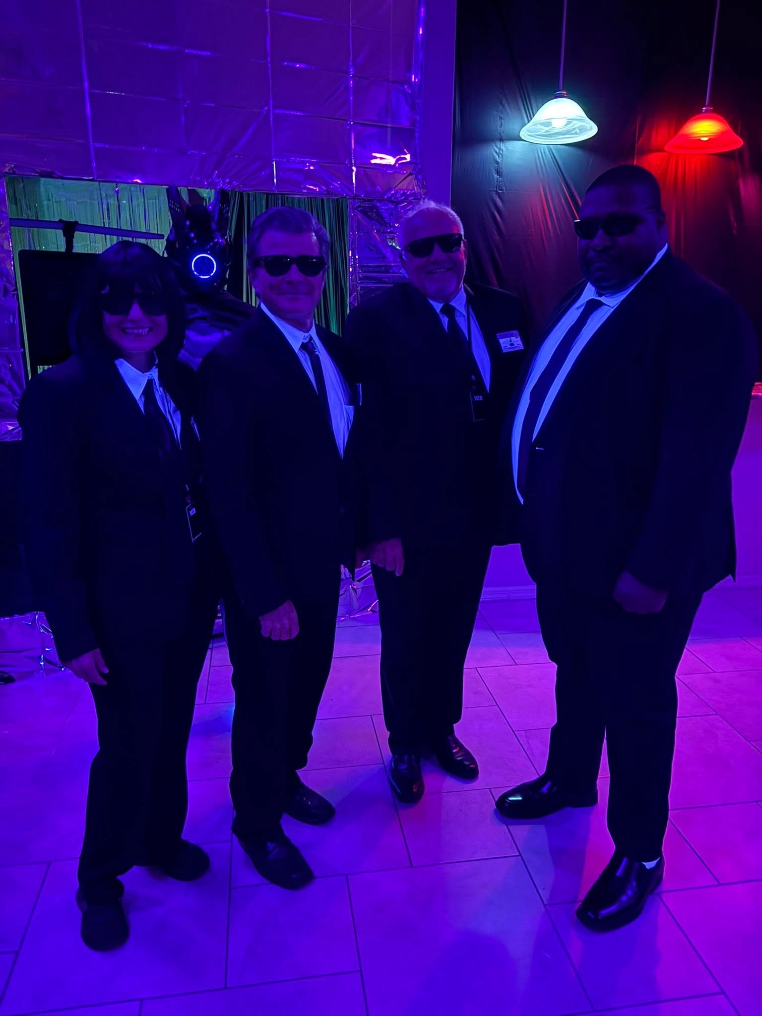 Four guests dressed like secret agents posing under blue and red lights at The Space Station in 2025