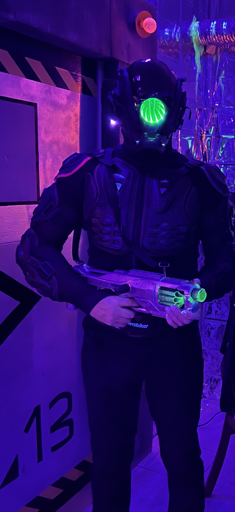 A futuristic armored figure holding a glowing blaster in the neon-lit station corridor at The Space Station in 2025