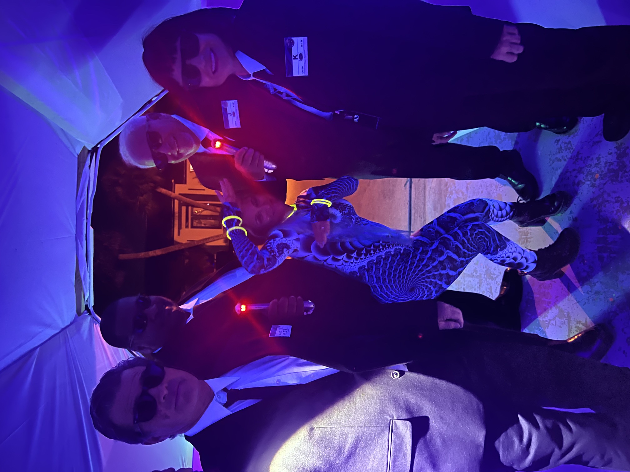 A group of guests including dark-suited agents and a glowing bodysuit entering through a bright portal tunnel at The Space Station in 2025